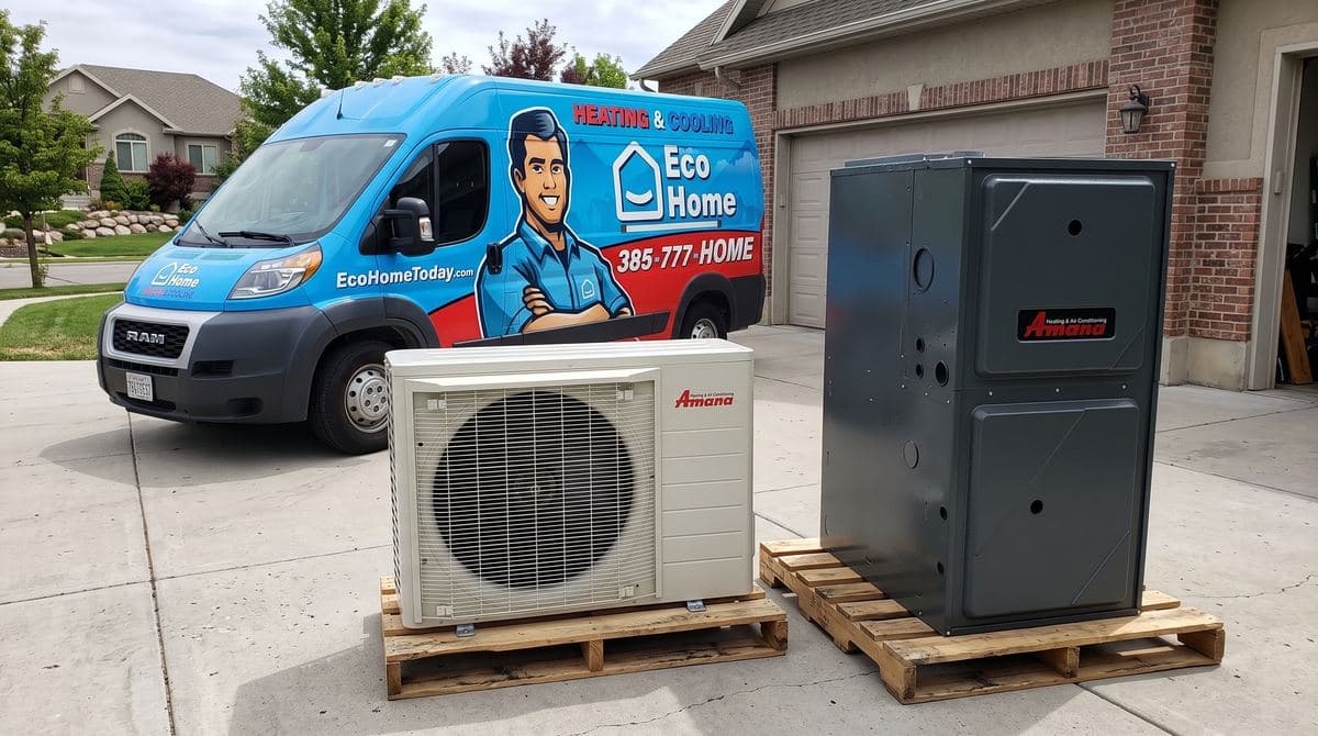 Side view of an Amana heat pump and gas furnace ready for installation, with the Eco Home van behind them