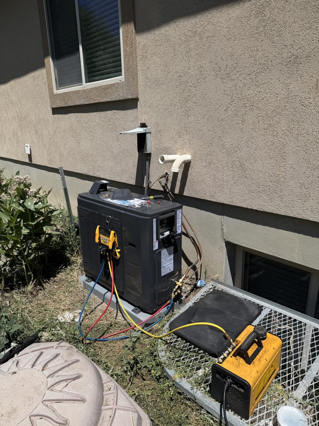 New inverter heat pump on its pad with gauges and a vacuum pump connected during an install