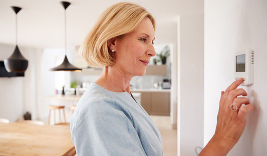 A woman adjusts the temperature on a wall, emphasizing energy efficiency in all-electric HVAC systems to manage energy costs.