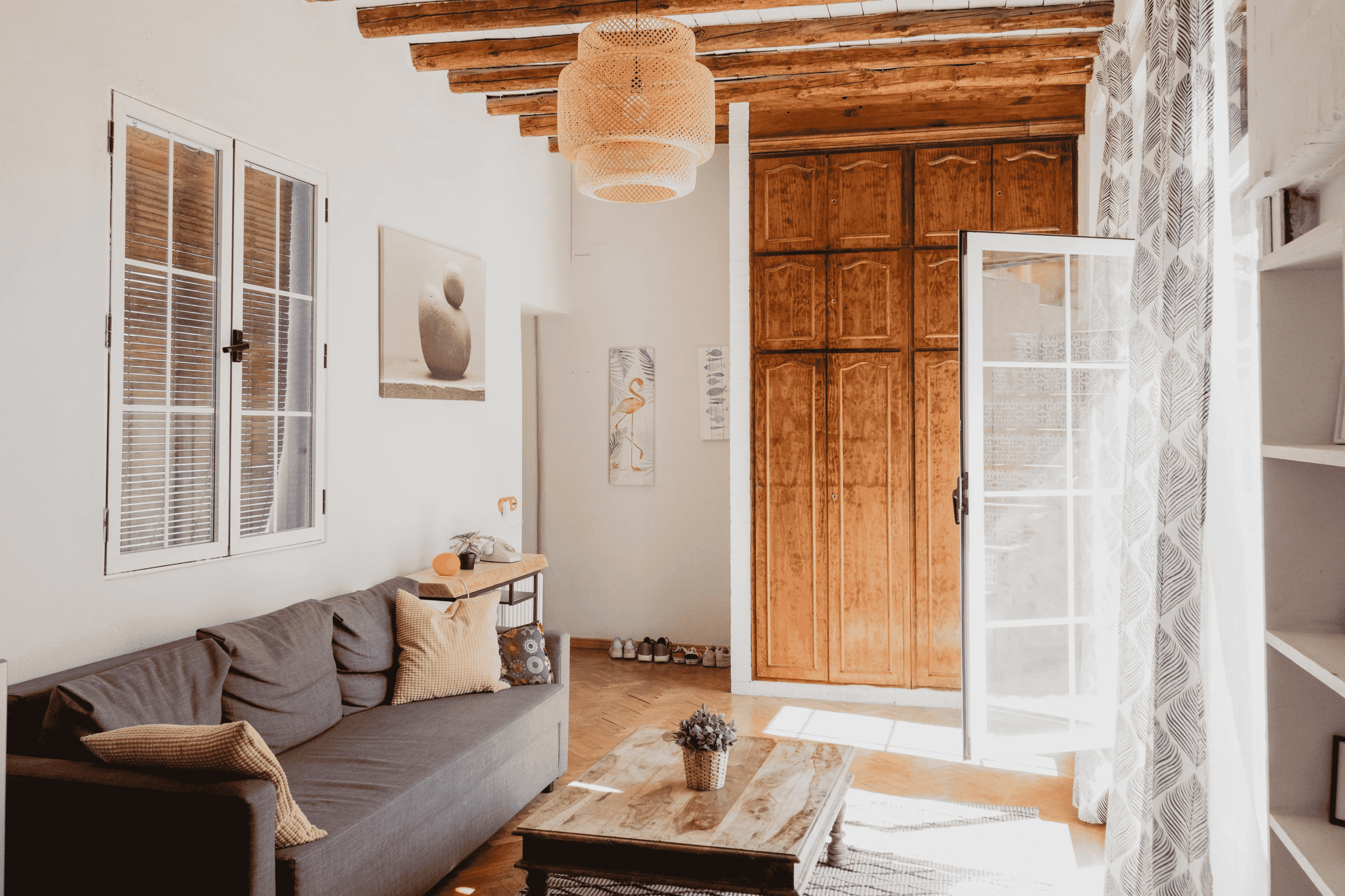 Cozy living room with a plush sofa, coffee table, and soft rug under a large window with sunlight streaming in.